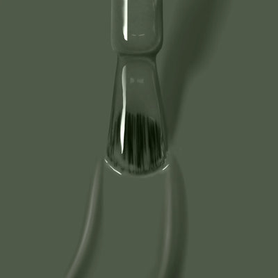 Close-up of a paintbrush dipped in gray liquid paint with bristles immersed and droplets on the handle, featuring the olive shade "Star Moss (Professional)" from LONDONTOWN's cruelty-free, vegan line.