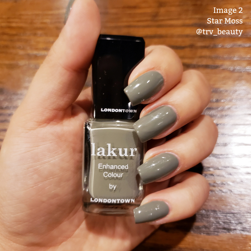 A hand with long, square-shaped nails painted in a glossy olive shade holds a bottle of LONDONTOWN Lakur nail polish labeled "Star Moss." This vegan cruelty-free polish is 16+ Free, ensuring a luxurious and ethical manicure.