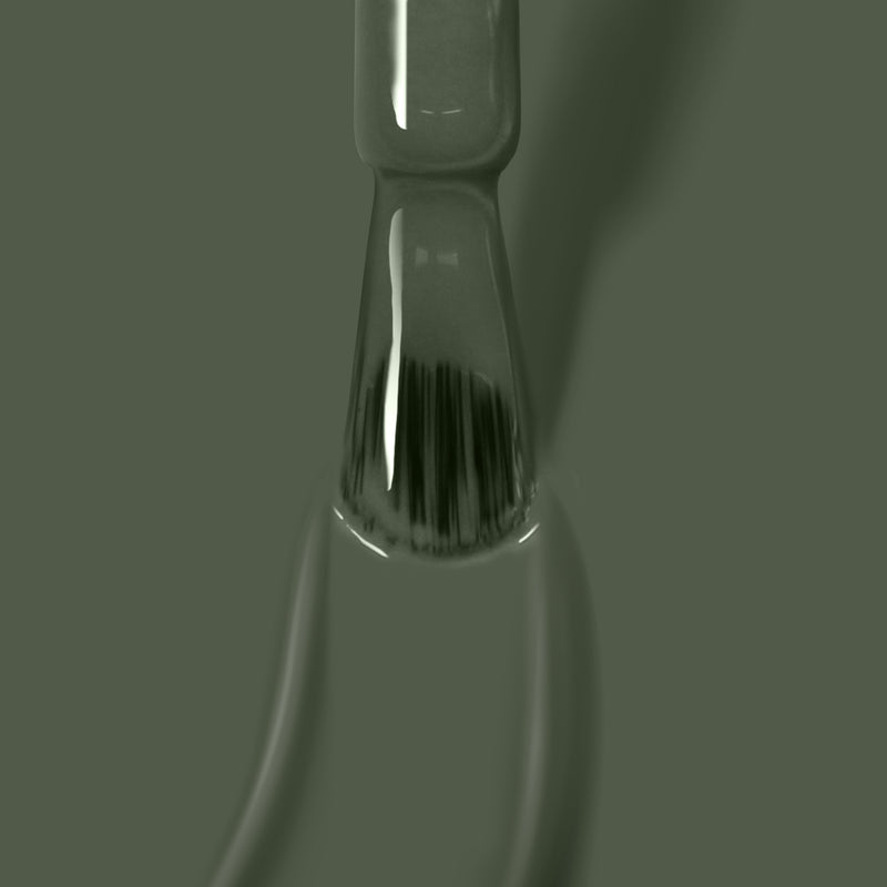 Close-up of a green paintbrush with bristles partially covered in an olive shade of Star Moss paint from LONDONTOWN, set against a green background.