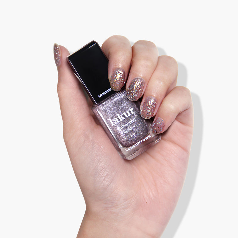 A hand with glittery, light purple nail polish holds a matching bottle labeled "lakur Enhanced Colour Starstruck by LONDONTOWN," featuring cruelty-free and vegan shimmer polish.