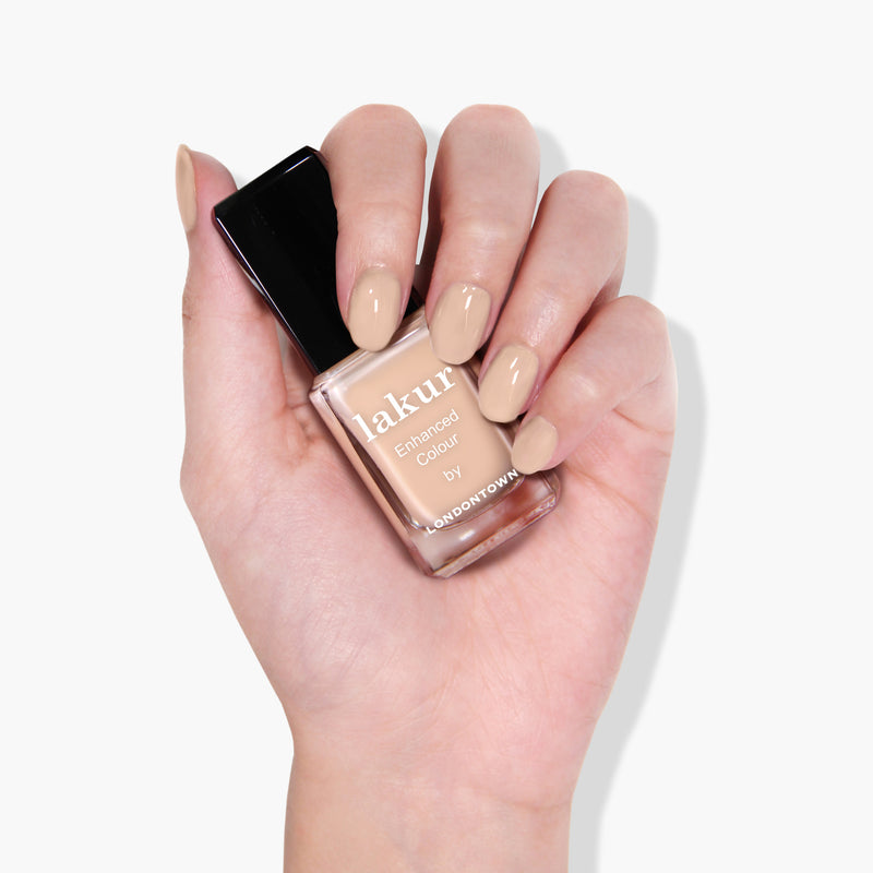 A hand holding a bottle of LONDONTOWN's Teatime nail polish, with nails painted in a cruelty-free sheer barely-there nude shade, perfect for an elegant afternoon tea.