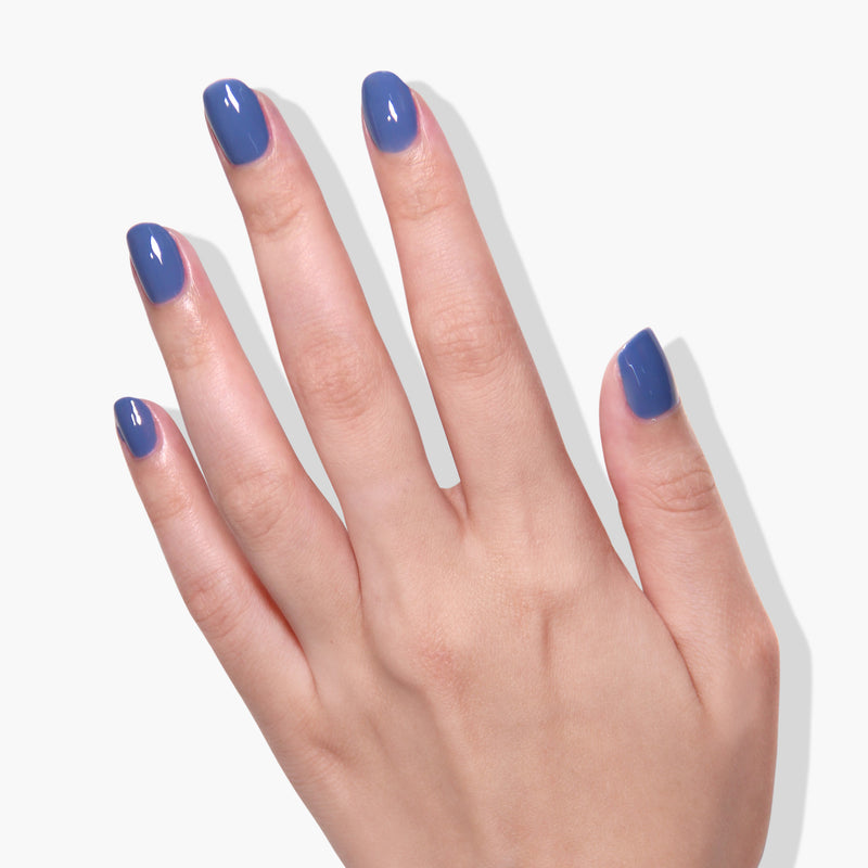 A hand with fingers extended, showcasing LONDONTOWN's shiny "To the Moon" crème blue gel color on well-manicured nails against a white background.