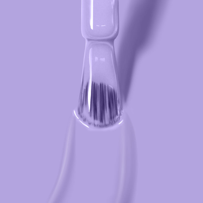 Close-up of a nail polish brush being pulled out of a bottle, dripping light purple Trolley Away nail polish by LONDONTOWN. The background is also light purple.