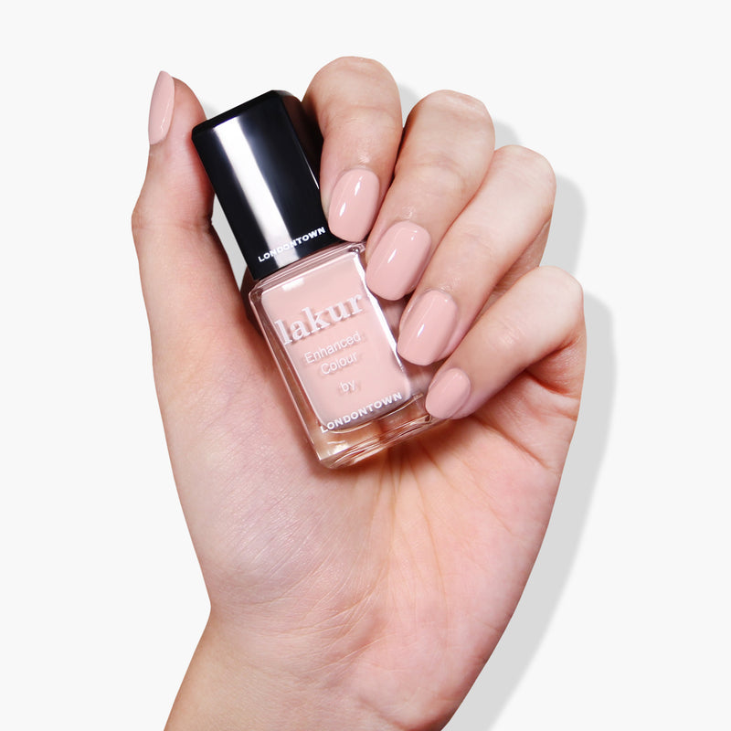 A hand holding a bottle of Uncovered nail polish by LONDONTOWN with matching nude polish painted nails.