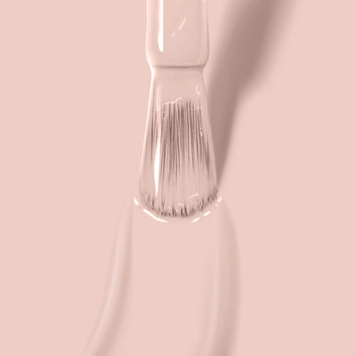 Close-up of a paintbrush applying LONDONTOWN's Uncovered (Professional) light beige polish on a surface.