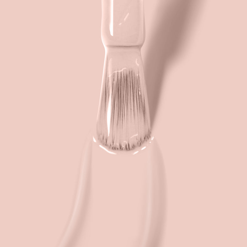 Close-up of a white paintbrush applying LONDONTOWN's Uncovered light pink paint on a smooth surface with a soft shadow in the background, blending seamlessly like nude polish.