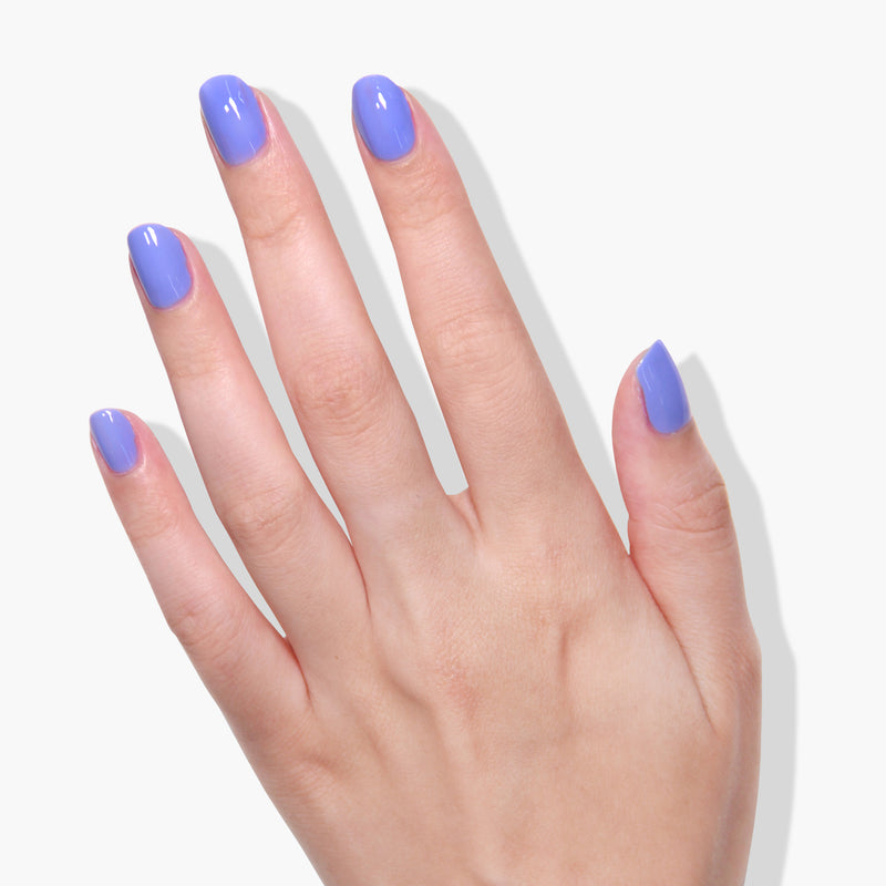 A hand with short, neatly manicured fingers is painted with LONDONTOWN's bold purple vegan nail polish, Uptown, against a white background.