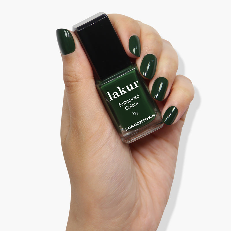 A hand with well-painted jade green nails holds a bottle of matching nail polish labeled "Vibe by LONDONTOWN.