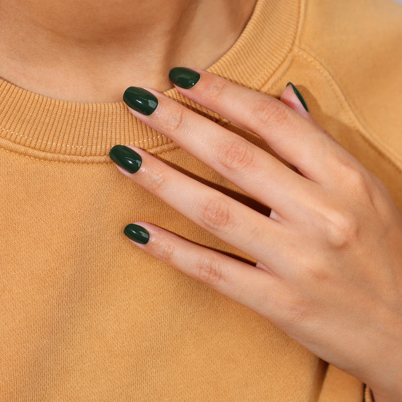 A hand with Vibe by LONDONTOWN jade green nail polish rests on a tan-colored sweater.