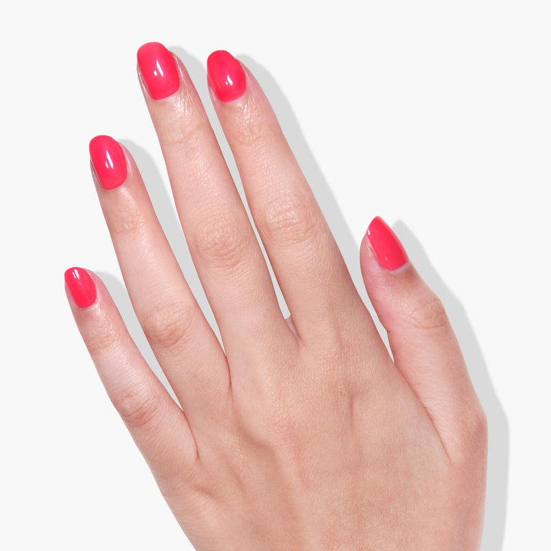 A close-up of a hand with short, neatly manicured nails painted in LONDONTOWN's vibrant coral pink crème gel color, Weekend Cheers, against a white background.