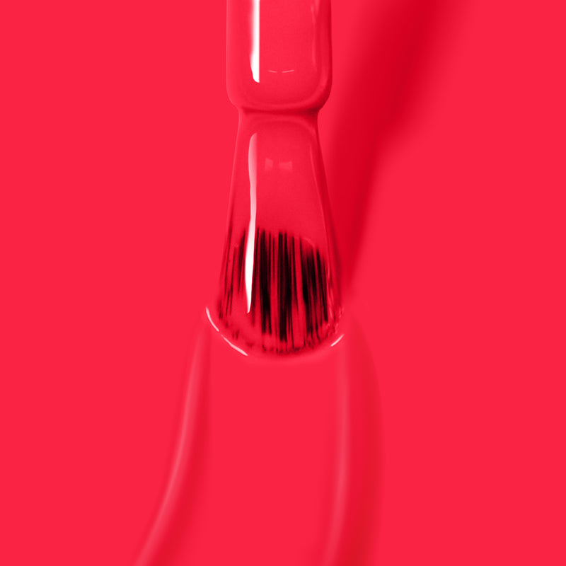 A close-up of a brush applying LONDONTOWN's Weekend Cheers coral pink crème nail polish on a surface.