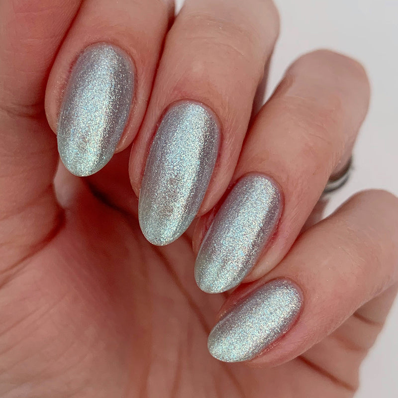 A hand displaying oval-shaped fingernails painted with a shimmering, metallic silver nail polish accented with ultrafine glitter from the Whipped Blueberry collection by LONDONTOWN.