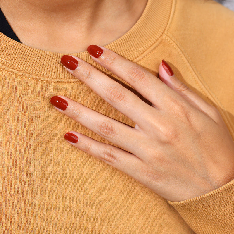 A hand adorned with manicured, sophisticated Woodstock nails from LONDONTOWN rests on a rich red-brown, mustard-colored sweater.