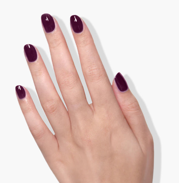 A hand with five fingers is shown adorned in LONDONTOWN's Bell in Time, a deep purple cream polish on each nail, set against a plain white background.