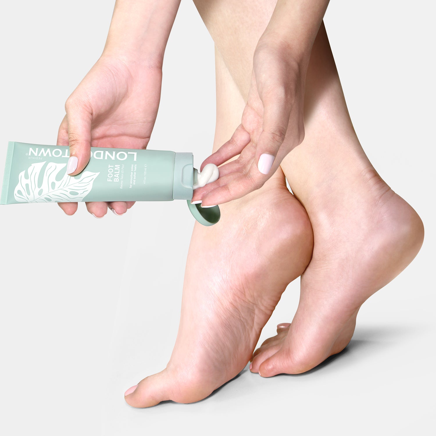 Person applying a Foot Balm with a lemongrass scent from a green tube labeled "LONDONTOWN" onto their foot.
