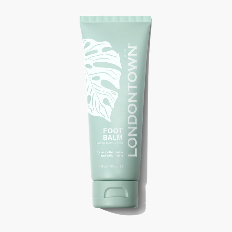 A tube of LONDONTOWN Foot Balm, featuring a green, leafy design and white text that highlights its benefits for smoother soles and softer heels. Infused with eucalyptus and lemongrass for a refreshing touch, this balm is available in a 4 fl oz (120 ml) size.