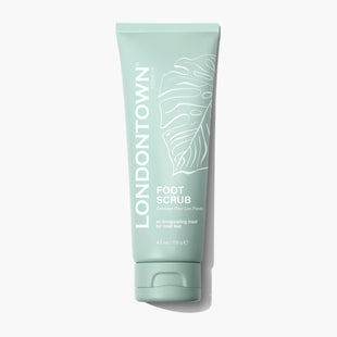 A green tube labeled "LONDONTOWN Foot Scrub," featuring a leaf design and containing 4.2 oz (120g). The text reads, "An invigorating treat for tired feet," highlighting its natural sugar crystals and essential oils.